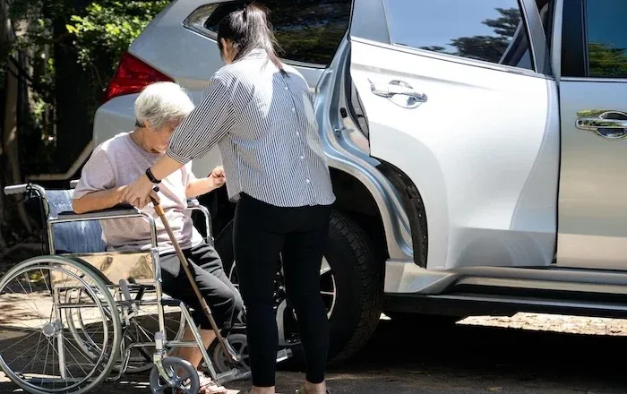 訪問医療、介護サービスの活用イメージ。車椅子の高齢女性が白いSUVに乗り込もうとしている様子。