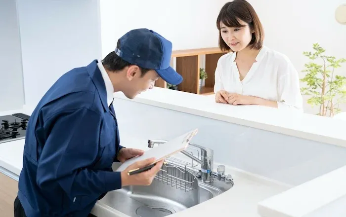 駆けつけサービスの活用イメージ。青いユニフォームのサービス技術者がキッチンで作業している様子。