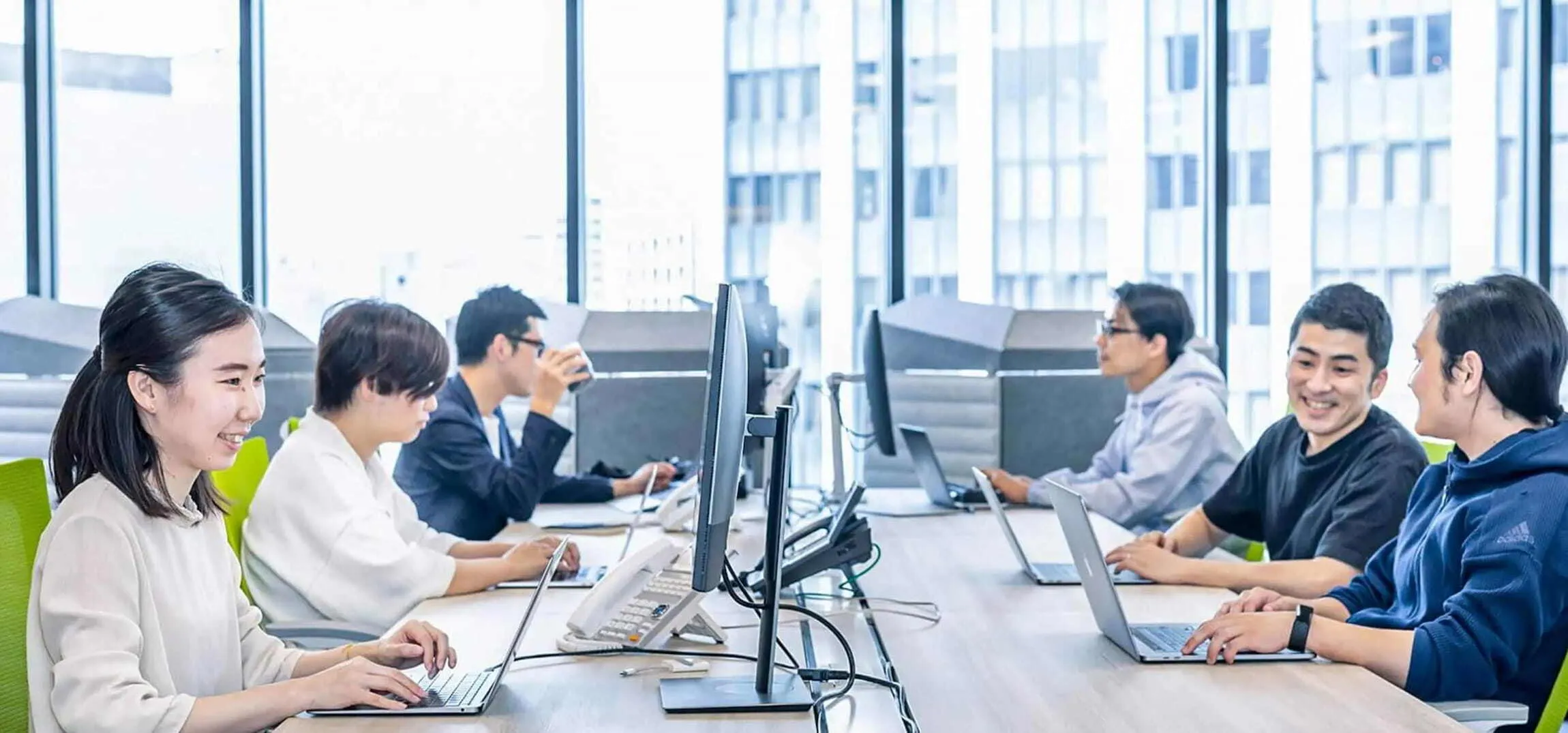 オフィスでデスクに座り、談笑しながら仕事をするシステム開発エンジニアたち