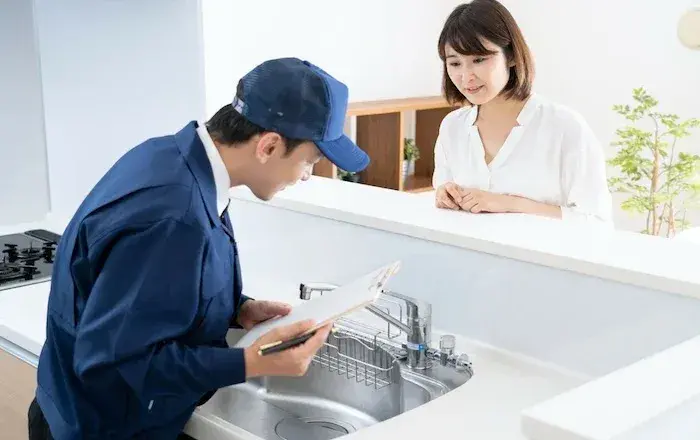 駆けつけサービスの活用イメージ。青いユニフォームのサービス技術者がキッチンで作業している様子。